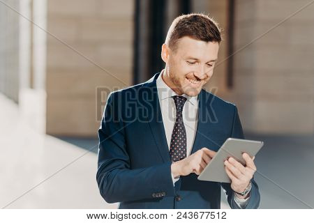 Happy Prosperous Businessman In Formal Wear, Makes Money Transaction Via Touch Pad, Has Glad Express