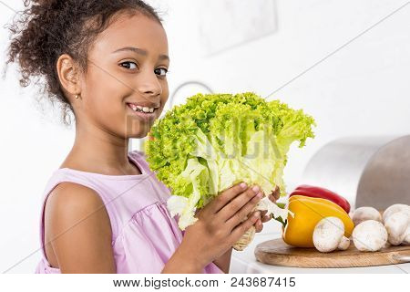 Smiling African American Child Holding Green Fresh Lettuce In Kitchen