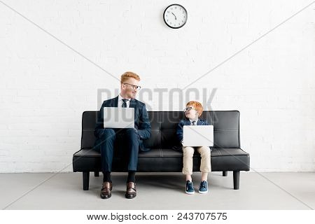 Smiling Father And Son Businessmen In Eyeglasses Using Laptops And Looking At Each Other