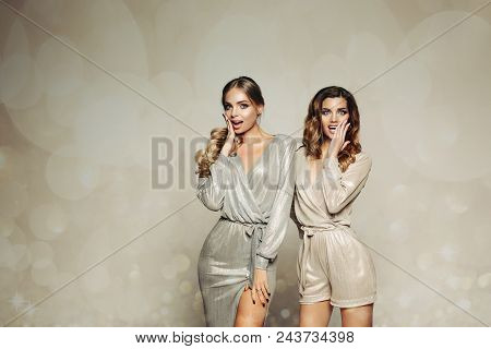 Two Glamrous And Beatiful Girls In Shiny Dress, Surprised Looking At Camera And Gesturing By Hands. 