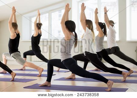 Group Of Young Sporty People Practicing Yoga Lesson, Doing Warrior I Exercise, Virabhadrasana 1 Pose