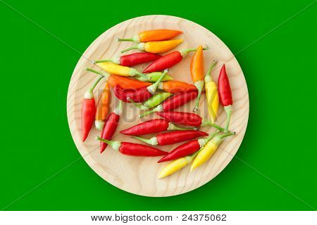 barevné chilli papričky deska izolovaná na zeleném pozadí