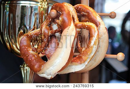 Close-up Of Fresh Baked Bavarian Pretzels Hanging On A Wooden Rack, With A Metal Sausage Pot In The 