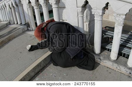 Old Gypsy Woman With A Black Jacket And A Shawl On Her Head Asking For Alms On A Bridge