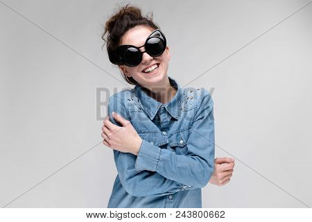 Young Girl In Black Cat Glasses On A Gray Background. Portrait Of A Young Beautiful Girl. Charming G