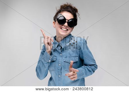Young Girl In Black Cat Glasses On A Gray Background. Portrait Of A Young Beautiful Girl. Charming G