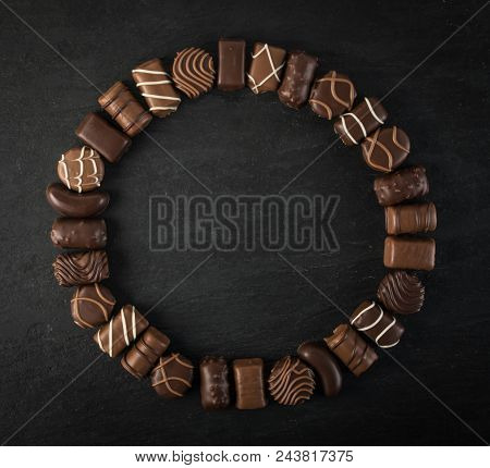 Beautiful Creative Chocolate Sweets On Natural Black Stone Background. Mix Of Chocolates In Round Fr