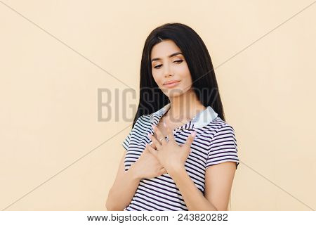 Indoor Shot Of Pretty Female Keeps Hand On Chest, Expresses Her Good Atitude To People, Has Long Dar
