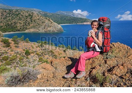 A Woman With Baby In A Sling And A Large Backpack Travels Along The Carian Path. Turkey