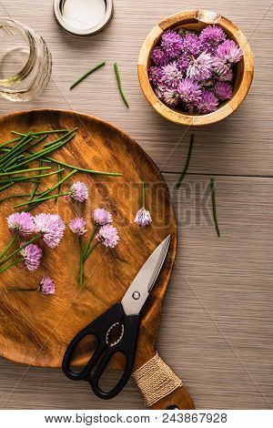 Over Head Photo Of Chives Blossoms Being Cut With Sissors From Stems And Placed In A Wooden Bowl.