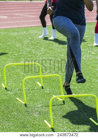 A Runner Is Performing Speed Drills Ovr Yellow Mini Banana Hurdles With No Shoes On During Trak And 