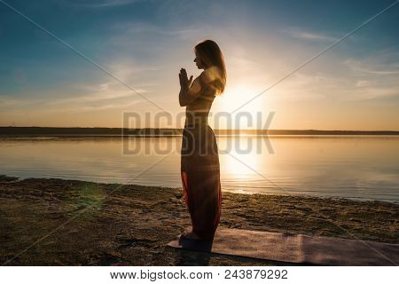 Silhouette Woman On The Beach At Sunset Doing Yoga Asana. Morning Natural Stretch Warm-up Training