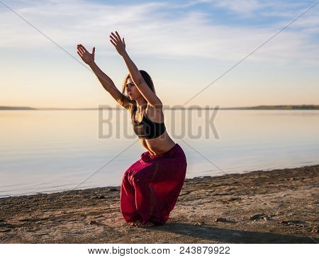 Silhouette Woman On The Beach At Sunset Doing Yoga Asana. Morning Natural Stretch Warm-up Training