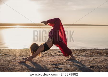 Silhouette Woman On The Beach At Sunset Doing Yoga Asana. Morning Natural Stretch Warm-up Training