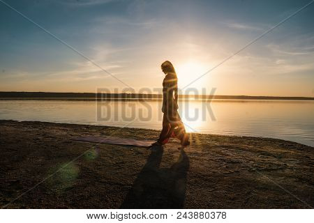 Silhouette Woman On The Beach At Sunset Doing Yoga Asana. Morning Natural Stretch Warm-up Training