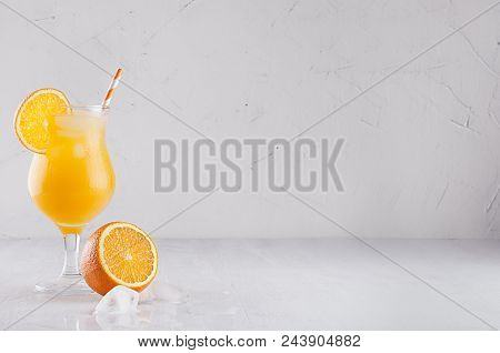 Yellow Cold Juice With Ice Cubes, Straw And Half Oranges On Soft White Plater Background.