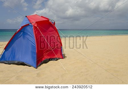 Red And Blue Tent On The Sandy Beach In Morro Jable On Fuerteventura. Turquoise Water Of The Atlanic