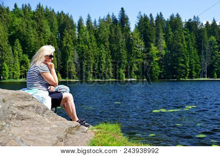 Woman sitting on rock by moraine lake Grosser Arbersee in National park Bavarian forest. Germany.