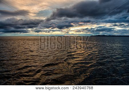 Sunset Over Stormy Clouds Across The Water Reflecting Dark And Looming Dramatic Sky Moody Feeling Of