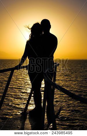 Silhouette Of Young Couple On Yacht Over The Orange Sea Sunset. Romantic And Love Concept.