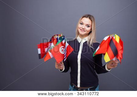 Cheerful Young Woman With A Large Set Of Flags Of Different Countries Of The World. Polyglot, And Le