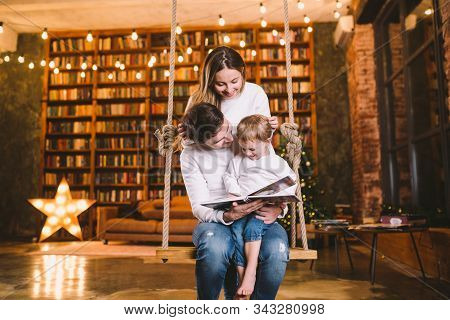 Family With Baby Relaxing On Home Swing Seat In Cozy Dark Living Room On Christmas Eve. Family Havin