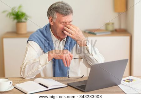 Eyestrain Concept. Elderly Businessman At Laptop Massaging Nosebridge Having Headache Or Sore Eyes S