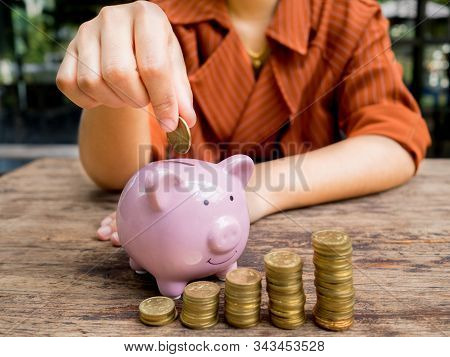 Business Woman Hand Putting Coin Into  Pink Piggy Bank With 
Gold Coins Pile Growth Graph, Saving Mo
