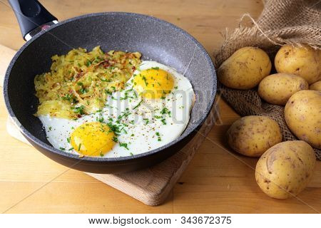 Fried Eggs And Swiss Roesti In A Pan On A Wooden Kitchen Table With A Sack Of Potatoes, Selected Foc