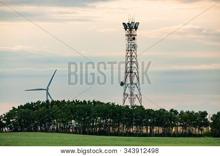 A Wide Angle Late Afternoon View Of A Cell Site Tower In A Lush Green Landscape With Woodland, Grass