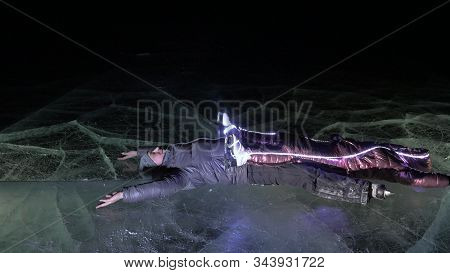 Young Loving Couple Skating At Ice Rink At Night. Man And Woman Kiss Hug Have Fun Learn To Skate. Ma