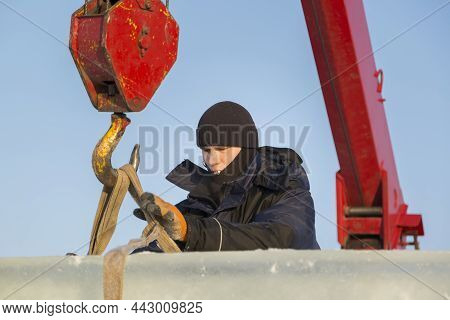 Portrait Of A Worker In A Blue Jacket With A Hood At The Hook Of A Truck Crane