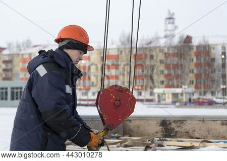 Portrait Of A Worker In A Blue Jacket With A Hood At The Hook Of A Truck Crane