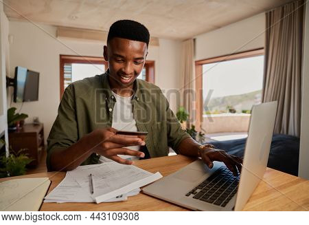 Happy Young Adult Black Male Smiling, Making Online Payment On Laptop In Modern Apartment.