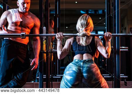 Sporty Sexy Couple With Barbell In Gym. Sportive Couple In Gym. Personal Trainer Helping Woman Doing