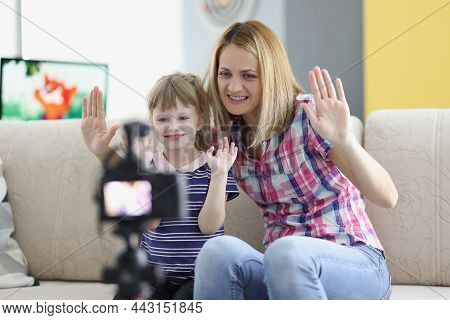 Portrait Of Mother And Daughter Wave Hello On Video, Videocamera Set On Tripod. Girl And Woman Have 