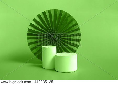 White Cylindrical Podium With Red, Green Paper Fan Background For Branding And Product Presentation.