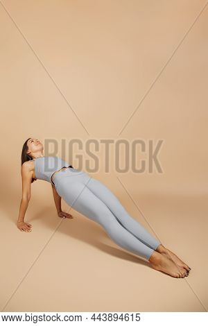 Brunette Is Engaged In Fitness. Beautiful Young Woman In Gray Tight-fitting Yoga Suit Does A Reverse