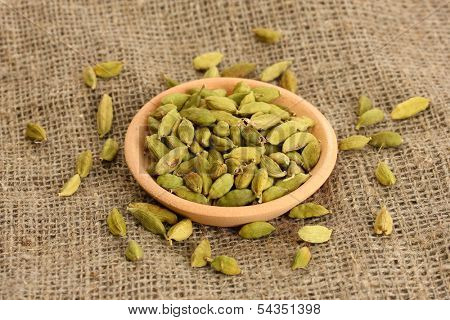 Green cardamon in clay bowl on canvas background close-up