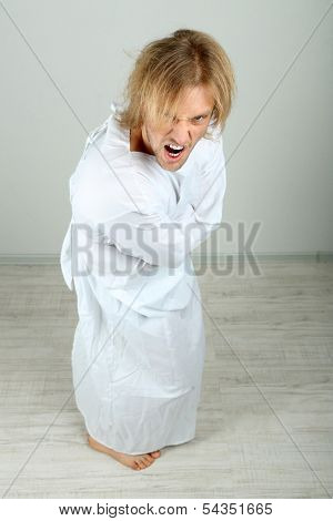 Mentally ill man in strait-jacket on gray background