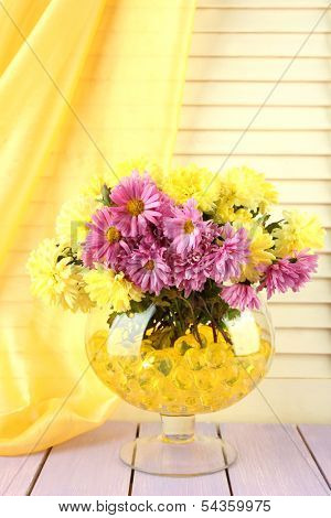 Beautiful flowers in vase with hydrogel on table on wooden background