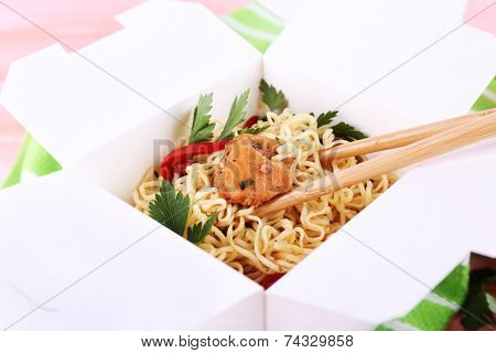 Chinese noodles and sticks in takeaway box on green napkin on pink background