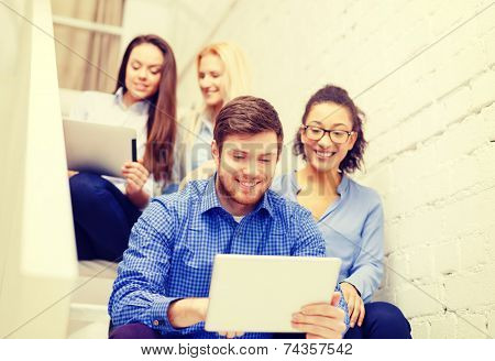 business, technology and startup concept - smiling creative team with tablet pc computer sitting on staircase