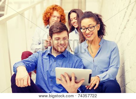 business, technology and startup concept - smiling creative team with tablet pc computer sitting on staircase