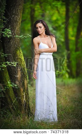 Lovely young lady wearing an elegant long white dress enjoying the beams of celestial light on her