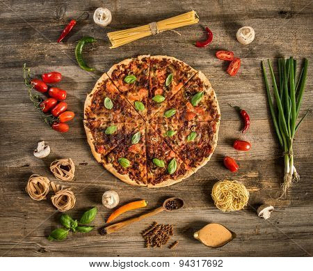 Italian food background with pizza, raw pasta and vegetables on wooden table