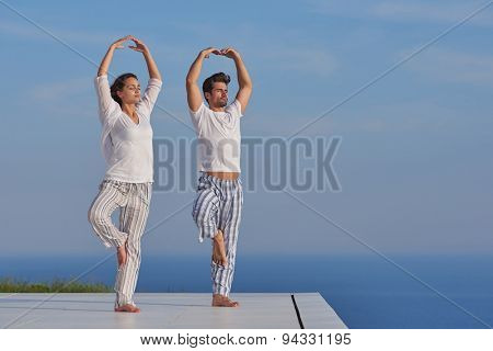 young couple practicing yoga at sunset in modern home terace with ocean and sunset in background