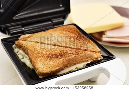 closeup of two sandwiches filled with ham and cheese toasted in an electrical sandwich toaster