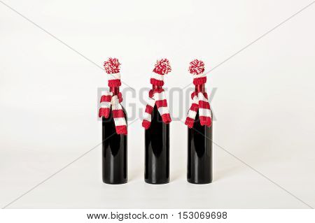 Merry Christmas and happy New year. Three bottles of wine in knitted caps and scarfs in red and white stripes on a white background. Selective focus.