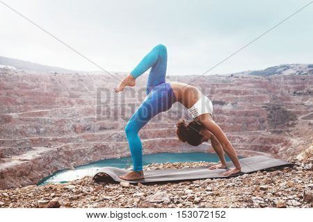 Young sporty girl wearing blue activewear stretching outdoors. Woman training yoga pose on mountain hill, calm and silent view.